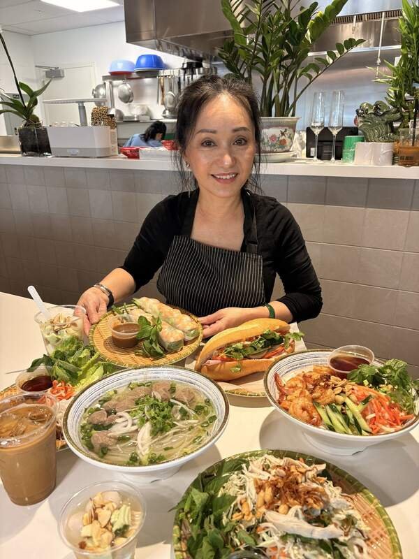 Mandy Nguyen at her counter inside Midtown Eats, with pho, banh mi, summer rolls, and Vietnamese iced coffee laid out in front of her